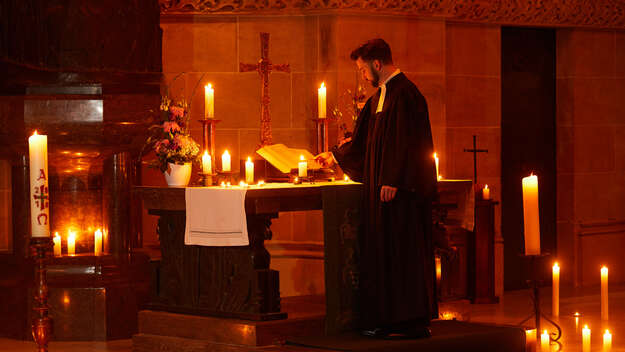 Ein Pfarrer steht in einer von Kerzen erleuchteten Kirche am Altar.