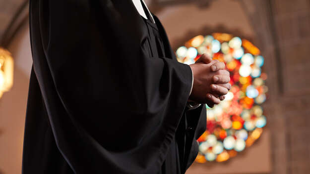 Pfarrer betet mit gefalteten Händen in einer Kirche.