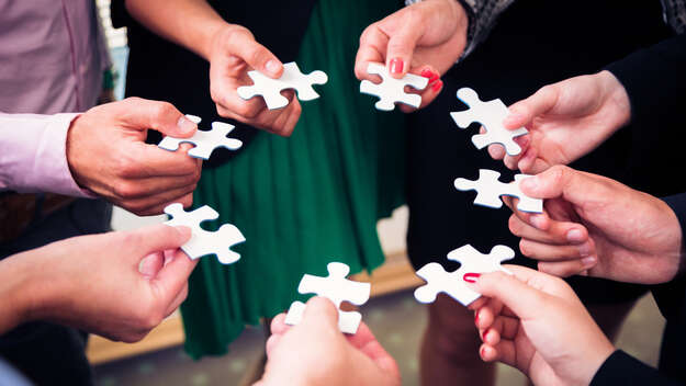 Nnahaufnahme einer Menschengruppe mit Puzzleteilen in den Händen.