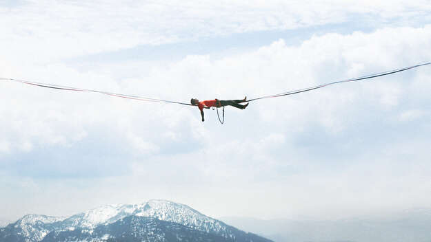 Ein Mann liegt in großer Höhe auf einer Slackline.