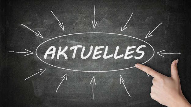 An einer Tafel steht mit Kreide 'Aktuelles' geschrieben, eine hand zeigt darauf