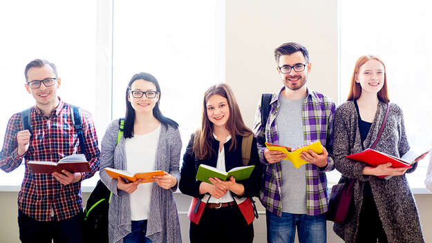 Schüler im Teenageralter stehen mit aufgeschlagenen Heften und Büchern in einer Reihe