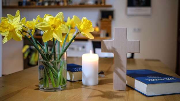 Symbolbild: Osterglocken, Kerze, Kreuz und Bibel für eine Andacht zu Hause