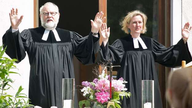 Pfarrer und Pfarrerin heben die Hände zum Segen am Altar