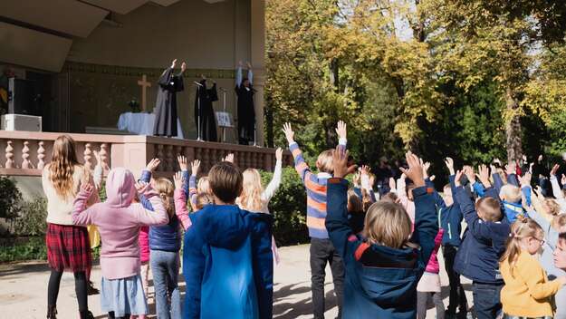 Bei einem Tauffest in Bad Homburg stehen Kinder mit erhobenen Armen vor der Bühne mit dem Altar und empfangen den Segen.