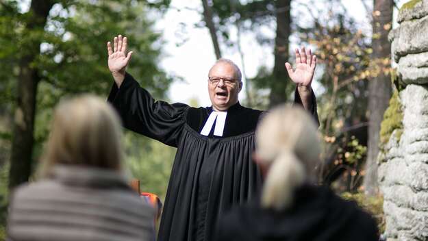 Dekan Thomas Guba hält bei einem Waldgottesdienst segnend die Hände hoch. Im Hintergrund