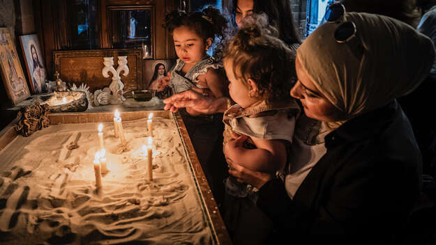 Eine Kirche in Homs, Syrien: Eine Frau (Christin) zeigt ihrer Freundin (Muslimin) die Kirche, gemeinsam mit ihren Kindern zünden sie Kerzen an.