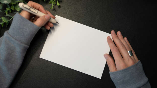 Zwei Hände, eine hält einen Stift, und eine unbeschriebene Postkarte