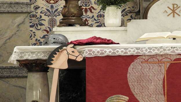 Ein Holzpferd lehnt am Altar einer Kirche. Ein Helm liegt ebenfalls darauf Ein Holzpferd lehnt am Altar einer Kirche. Ein Helm liegt ebenfalls darauf