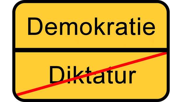 Symbolbild: Ein Straßenschild, auf dem Demokratie steht, darunter durchgestrichen Diktatur