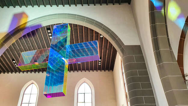 Lichtkreuz von Ludger Hinse in der Stadtkirche Darmstadt. Ein halb transparentes, bunt schillerndes Kreuz.