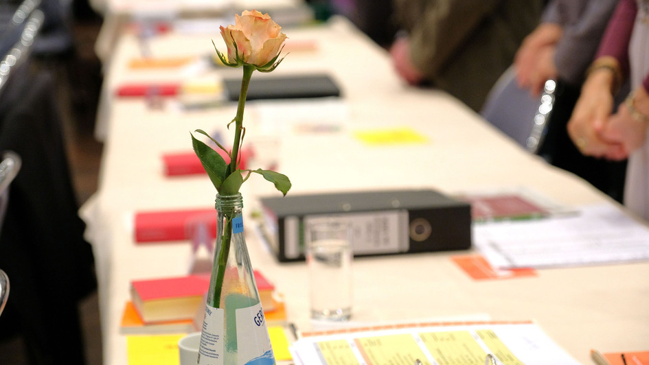 Schnappschuss von der EKD-Synode in Würzburg; langer Tisch mit Unterlagen, im Vordergrund eine Rose in einer Blumenvase