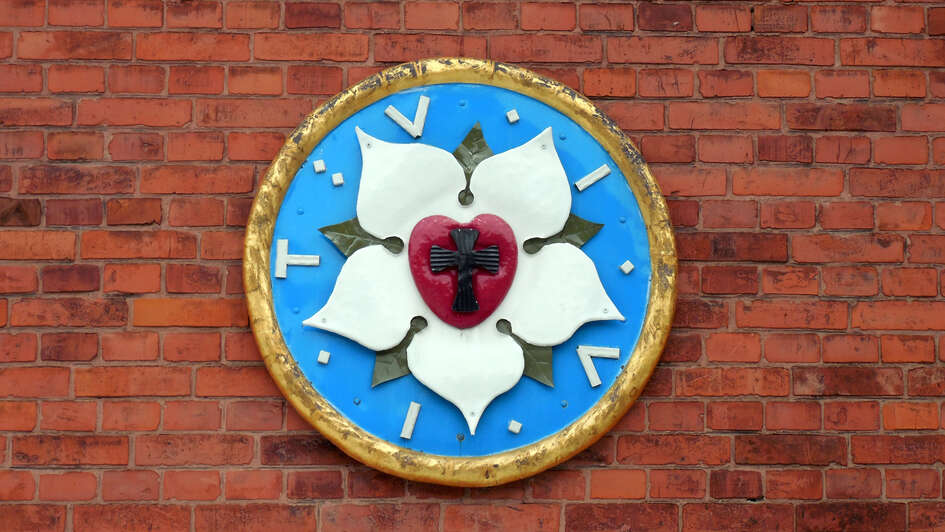 Eine Lutherrose auf einer roten Backsteinwand.