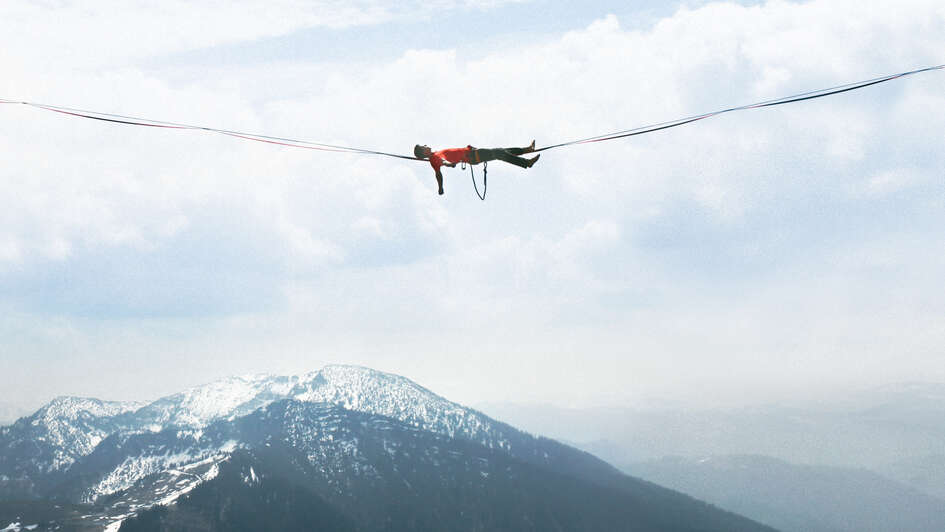 Ein Mann liegt in großer Höhe auf einer Slackline.