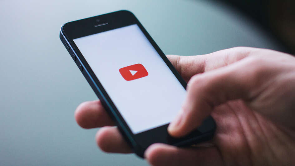 Eine Hand hält ein Smartphone mit Youtube-Logo