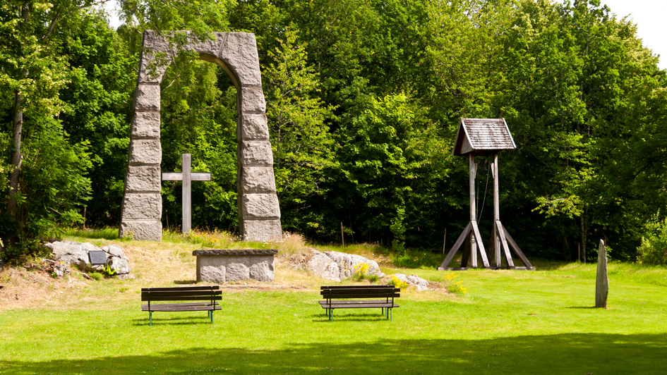 Bänke draußen vor einem Kreuz in einem Steinbogen