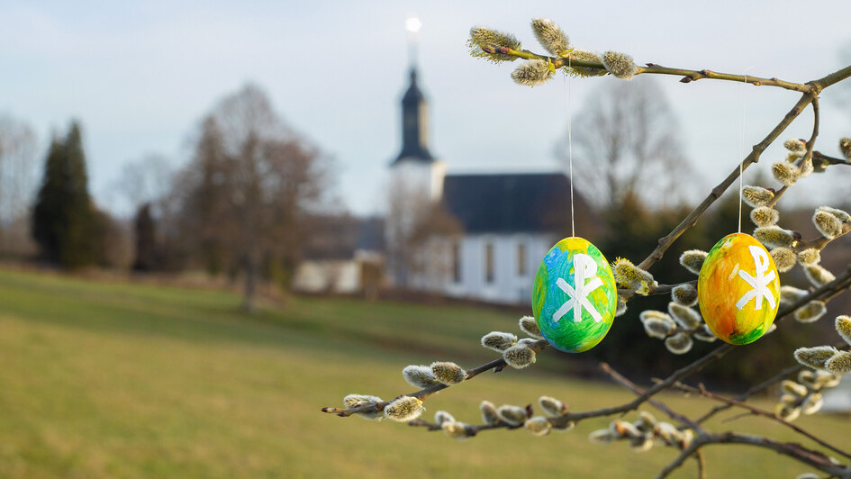 Im Hintergrund eine Kirche, im Vordergrund Ostereier an einem Strauch