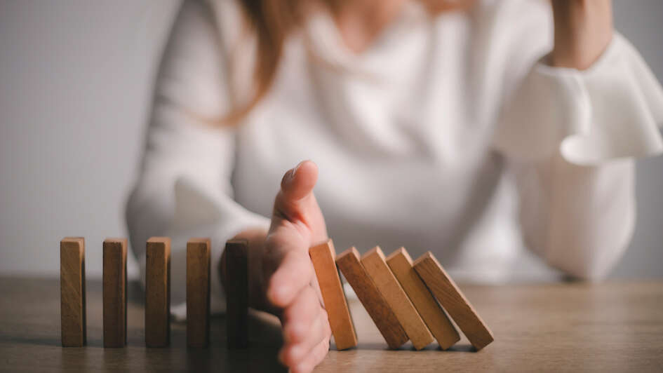 Symbolbild: Hand schützt Dominosteine vor dem Umfallen