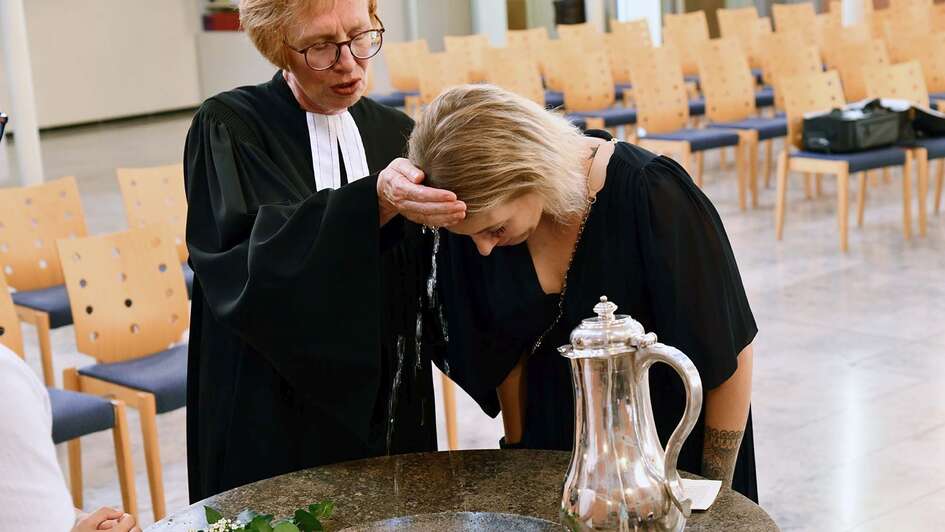 Die Hanauer Pfarrerin Margit Zahn tauft eine junge Frau am Taufstein mit Wasserkanne