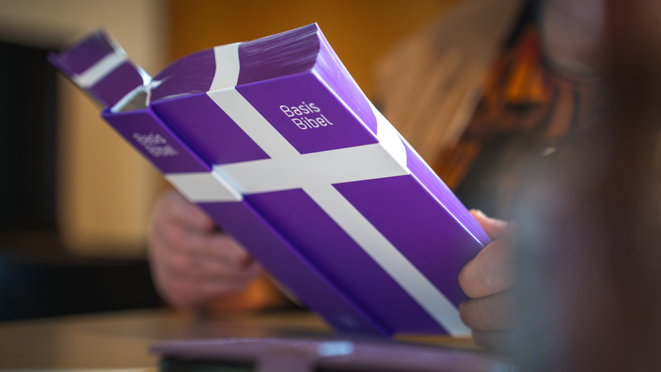 Die aufgeschlagene Basisbibel in den Händen einer Person