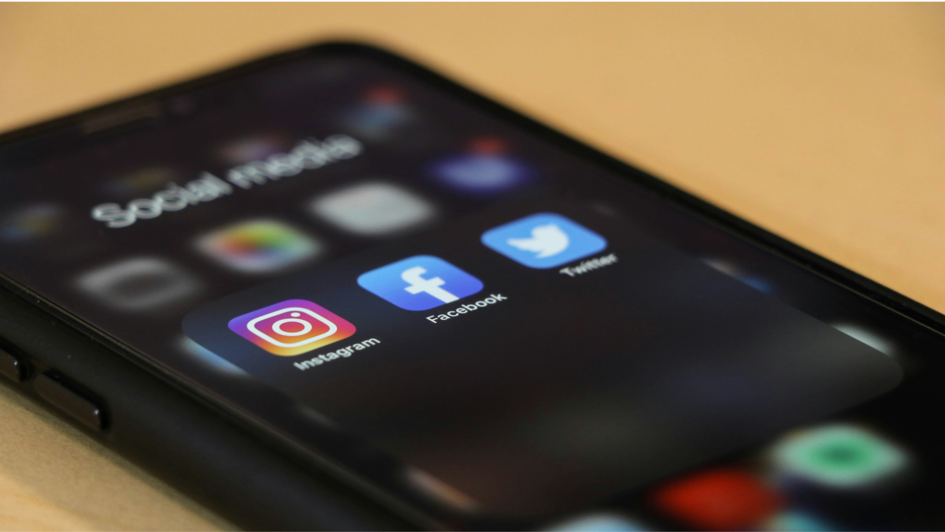 Nahaufnahme eines Smartphone-Bildschirms mit geöffnetem Ordner „Social Media“, in dem die Icons von Instagram, Facebook und Twitter sichtbar sind. Der Bildschirm ist leicht unscharf im Hintergrund, die App-Symbole im Fokus.