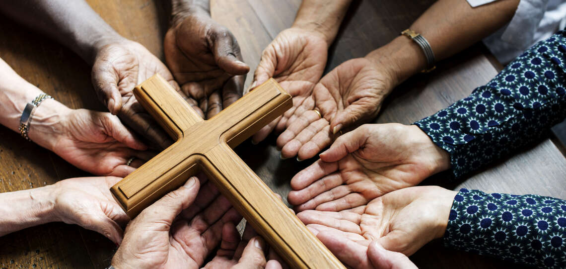 Mehrere Hände unterschiedlicher Hautfarben halten ein Holzkreuz