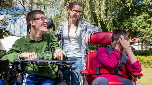 Eine junge Frau zwischen zwei Personen im Rollstuhl