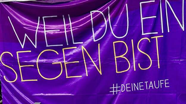 Auf einem violetten Stoff steht der Schriftzug: Weil du ein Segen bist #DEINE TAUFE