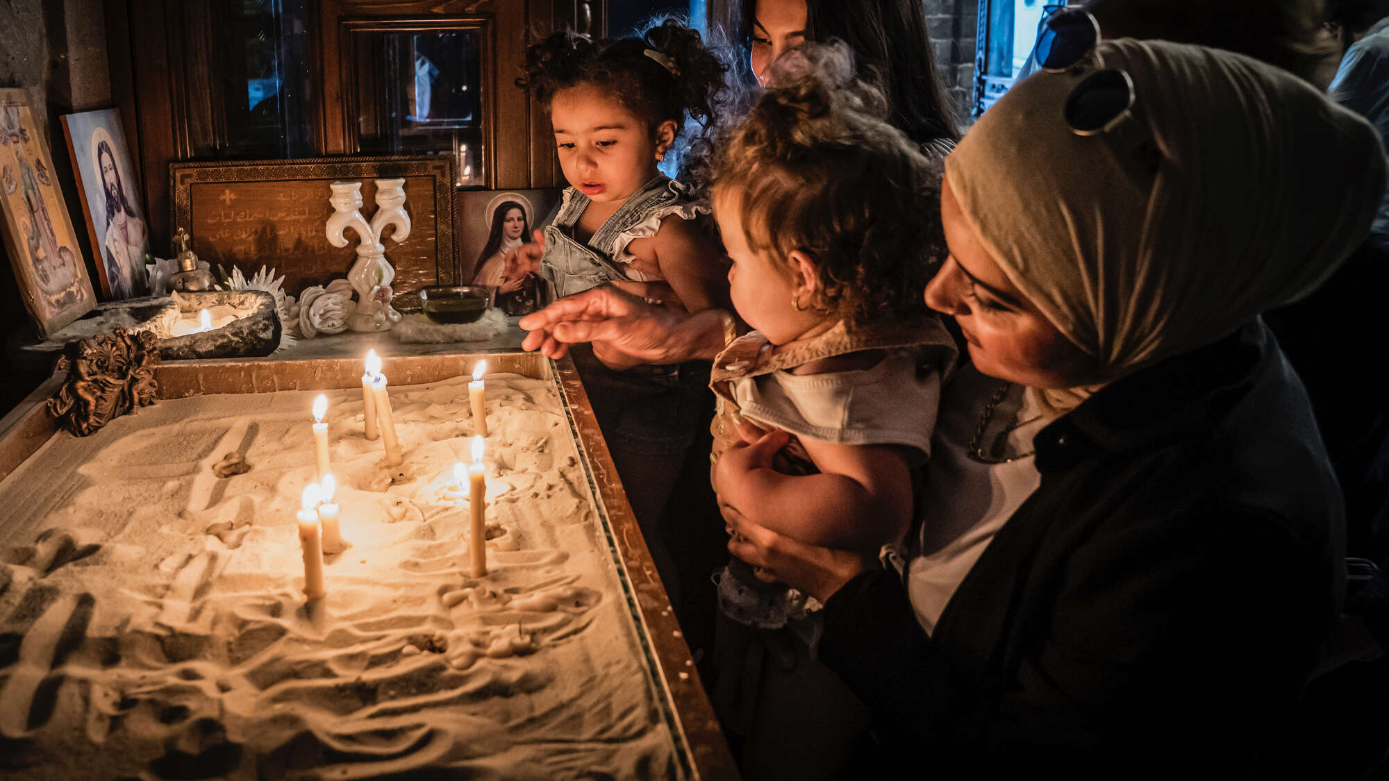 In einer Kirche in Homs, Syrien: Eine Frau (Christin) zeigt ihrer Freundin (Muslimin) diese Kirche, gemeinsam mit ihren Kindern zünden sie Kerzen an.
