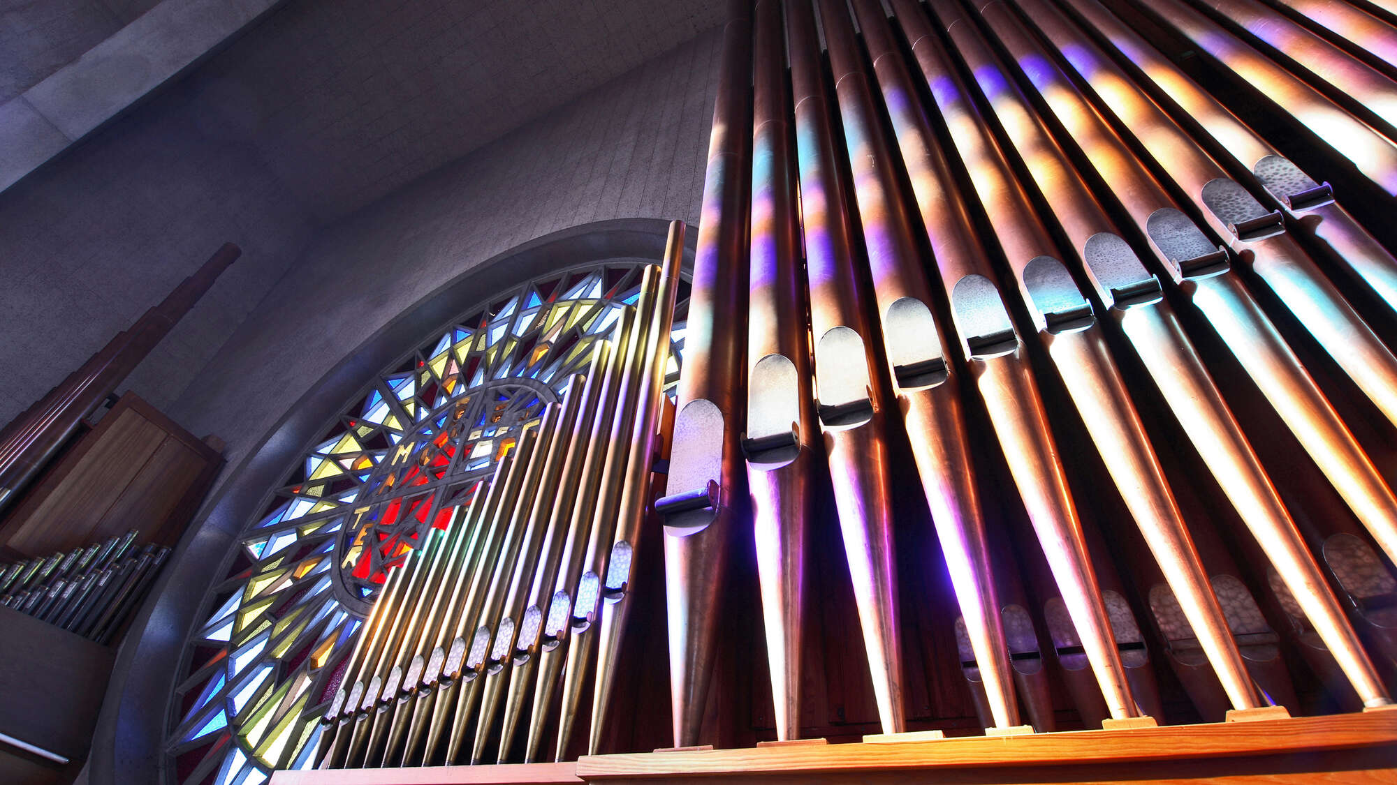 Orgelpfeifen neben einem Buntglasfenster in einer Kirche.