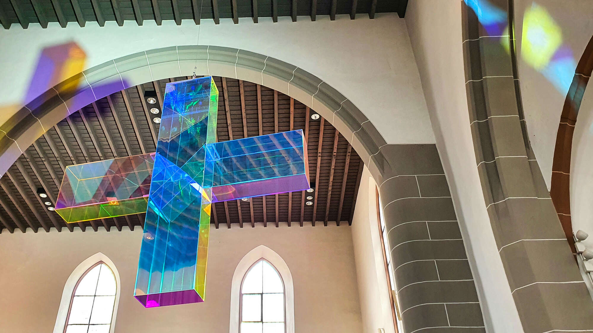 Lichtkreuz von Ludger Hinse in der Stadtkirche Darmstadt. Ein halb transparentes, bunt schillerndes Kreuz.