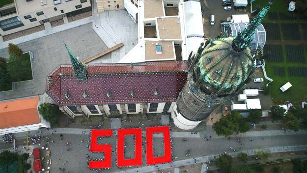 Luftaufnahme der Schlosskirche Wittenberg, vor der viele Menschen zusammen eine rote 500 aus Stoff halten.